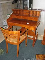 Teak captain's desk and wicker wood chair shown from an angle, highlighting carved details and chair's cane seat.