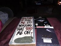 Photo showing the golf-themed sign and the 8-pack screen protector package together on a bed.