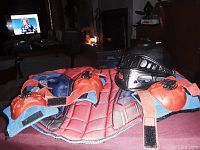 Photo of Spider-Man themed child protective gear including knee pads, elbow pads, chest protector, and black helmet on red surface.