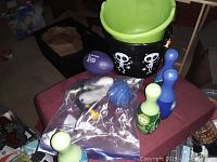 Image showing children's toy bowling set with green bucket, four bowling pins in blue and green, purple football, and small toy accessories in clear bag.