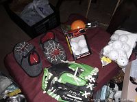 Photo of two pairs of boys Spider-Man themed shoes, green and black baseball glove, box of 3 table tennis balls, orange training ball, and bag of white wiffle balls on a red surface.