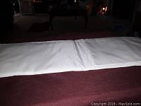 Close-up image of white fabric projection screen laid on a burgundy surface, showing its texture and fold.