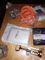 Overview photo showing mixed lot items on a table including swaddling blanket in white packaging, silicone wristbands, corkscrew, figurines, and other sealed items.