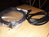 Two black cords on a wooden surface, one coiled in a plastic bag, the other loose with a ferrite bead.