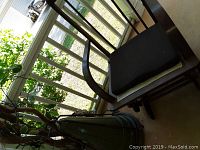 Old wooden rocking chair on porch with curved armrests and black seat cushion, missing vertical slats on backrest.