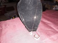 Necklace displayed on a black velvet stand with a teardrop pendant and matching ring size 6 placed in front on a red fabric surface.