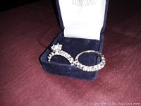 Silver wedding ring set with clear stones displayed in a blue velvet jewelry box on a red fabric surface