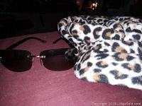 Leopard print cap and rectangular dark lens sunglasses on a reddish surface.