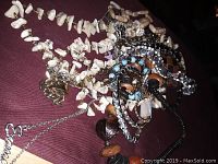 Lot of assorted jewelry including various necklaces and bracelets made of different materials such as shells, wood, beads, rhinestones, and chains placed on a dark surface.