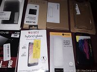 Photo showing a variety of phone cases and packaging for hybrid glass screen protectors from brands including Invisible Shield, Humixx, and Octane.