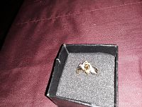 Gold-tone praying hands ring displayed in black cushioned jewelry box on a maroon fabric background.