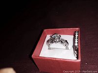 Engagement-style ring and wedding band displayed in a red jewelry box on dark surface.