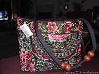 Side view of the floral embroidered pocket book showcasing its intricate design and wooden bead accents on strap.