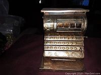 Front view of vintage tin toy cash register showing metallic finish, number windows and lever.