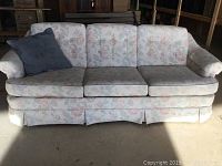 Front view of the floral-patterned queen sofa bed with three seat cushions and a dark grey pillow on the left armrest.