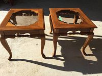 Pair of two solid wood end tables with smoke-colored beveled tempered glass tops and curved legs shown from above in sunlight.