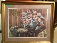 Framed floral print with bouquet of pink and purple flowers, ceramic vase, decorative plate, and table setting.