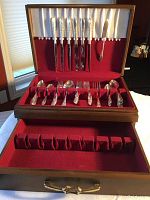 Open wood chest showing silver plate knives and forks held in place by velvet slots and loops in the chest lid and bottom tier