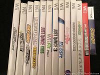 Photo showing 12 Wii game cases with titles visible, including Need for Speed Undercover, NASCAR Pro Street, Ski-Doo Challenge, Monster Jam, Just Dance series, Wii Fit Plus, Wii Sports Resort, Mario Sports Mix, and New Super Mario Bros Wii.