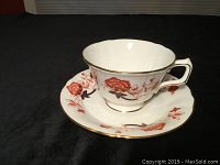 Tea cup with floral Bali pattern on white bone china, gold trim around cup edges and handle, placed on matching saucer