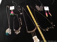Full view of 5 necklaces and 5 pairs of pierced earrings displayed on black background with measuring tape for size reference
