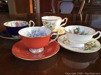 Four tea cups and saucers displayed on table showing different floral patterns and shapes