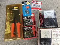 Rivet gun in packaging, assorted rivet packs, and Micronta multimeter on grey surface