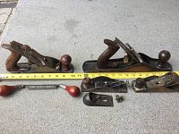Four Stanley wood planes arranged with measuring tape showing length. Visible surface rust on metal parts and wooden handles.