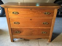 Front view of the small wood three-drawer dresser with brass handles and keyholes.
