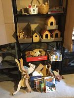Wide view of shelving showing multiple wooden birdhouses, assorted wooden blocks, a wooden animal-shaped toy, and craft books on bottom shelf.