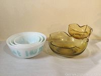 Photo of three white Pyrex nesting bowls with turquoise decoration next to two yellow glass bowls (chip and dip set)