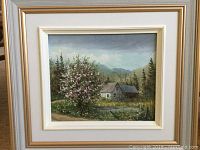 Framed oil on canvas painting showing a country landscape with house, trees, pond, and mountains.