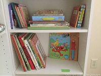 Shelf of vintage children's books arranged upright and stacked, titles visible include some hardcover and paperback books.