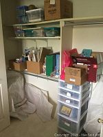 Wide view showing shelving with boxes, bins, and plastic drawers filled with assorted craft supplies including cards, papers, and ribbon rolls.