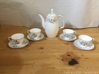 Wide view showing entirety of tea set including teapot, four cups, and their matching saucers arranged on wooden surface.