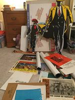 Photo of assorted movie posters, promotional paper items and standees on carpeted floor in front of wooden drawer set.