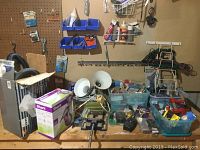 Wide view showing boxed Shark steam cleaner, Dirtbuster vacuum, lamps, clamps, and assorted hardware on table and pegboard.