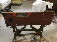 Front angled view of Deluxe Workmate wooden folding workbench showing visible wear and two orange clamps on top edge.