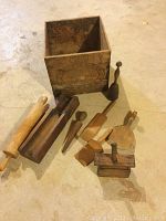 Photo showing entire set from a front angle including butter box, rolling pin, two comb-like butter spreaders, butter press, and other utensils on concrete floor.