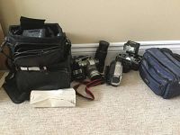 Full lot view with cameras, lenses, camera flash, charger, and bags on floor.