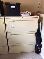 Full view of the neutral beige 3 drawer lateral file cabinet with items on top and a label on the front.