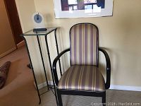 Full view of the side chair next to the glass top side table against a beige wall.