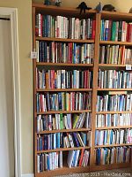 Front view of tall solid maple bookcase fully loaded with books.