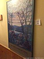 Framed poster "The New American Wing" displayed on wall with visible floral and mountain artwork under glass