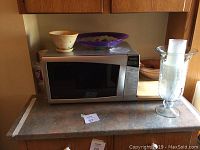 Microwave and surrounding countertop items including plastic bowls, cups, and cutting boards visible