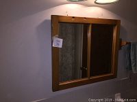 Front view of a rectangular mirror mounted in a pine window frame with three vertical sections, showing the natural wood frame and reflection.