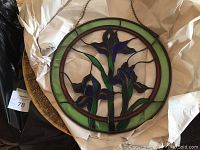 Two stained glass irises panels stacked flat with one brass tray visible underneath, wrapped in white tissue paper