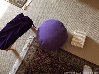 Photo shows purple round meditation cushion, wooden bench with fabric cover, and open decorative wooden box with ABC text on lid on carpeted floor.