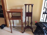 Two wooden side tables standing side by side against a wall, square one on left with shelf and turned legs, round one on right with twisted spindle legs and drawers.