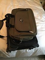 Top view of two stacked bags: olive green briefcase on top, black wheeled carry-on below, showing size comparison and zippers.